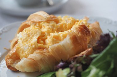 Taze salatanın yanında çırpılmış yumurtayla dolu lezzetli kruvasan..