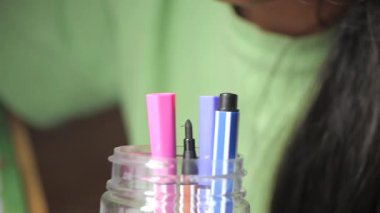 Colorful markers are being organized in a jar on a desk.