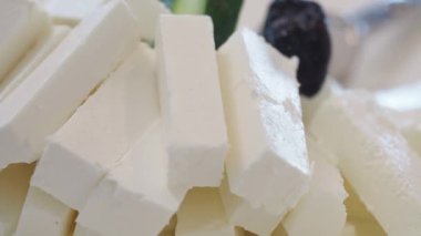 Slices of creamy cheese are arranged with fresh vegetables and olives.