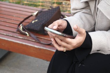 Parktaki bankta oturan bir kadın akıllı telefonuyla meşgul oluyor..