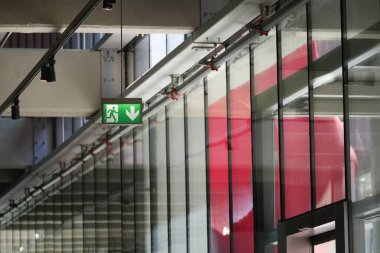Parlak acil çıkış işareti, cam duvarlı çağdaş bir koridoru aydınlatıyor..