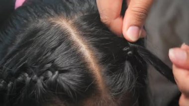Yetenekli bir bireyin parlak siyah saçlarda zarif örgüler oluşturmasını izle..