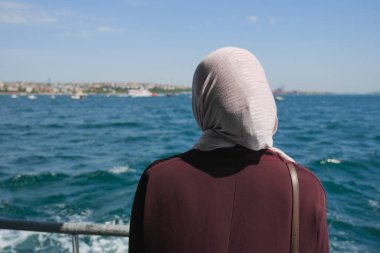 Başörtülü bir kadın bir tekneden denize bakıyor..
