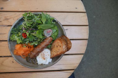 Haşlanmış yumurta, füme sosis, taze yeşillikler ve kızarmış ekmek..