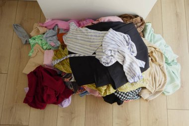 Ahşap zeminde rengarenk bir elbise yığını sıralanmayı bekliyor..