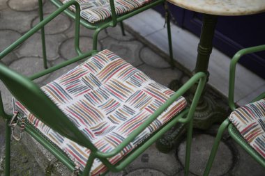 Açık hava kafe alanındaki bir masayı çevreleyen renkli yastıklı sandalyeler..