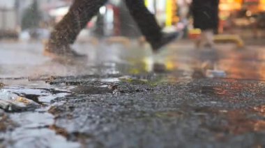 Yayalar yağmurun ardında parlayan su birikintilerini bırakarak işlek bir caddede yol alırlar..