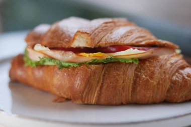 Marul, domates ve jambonla dolu bir kruvasan beyaz bir tabakta oturur..