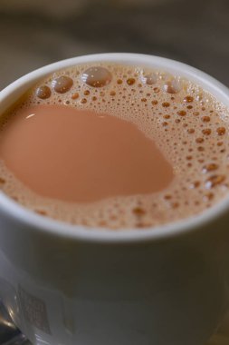 Bir fincan bol köpüklü çay bir masada duruyor, sıcaklığı ve lezzeti davet ediyor..