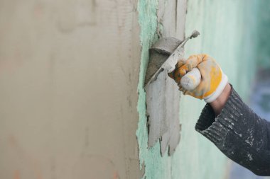 İnşaat işçisi duvarda bir malayla sıva yapıyor..