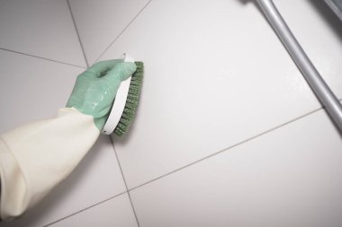 Eldiven giyen bir insan banyoda fırçayla fayans temizler..