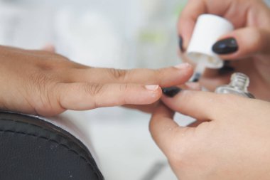 Bir tırnak teknisyeni müşterisinin tırnaklarına oje sürüyor..