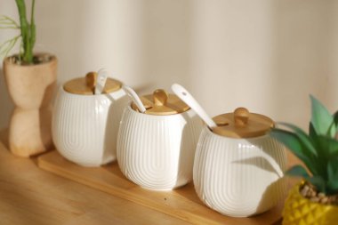 Tahta kapaklı üç beyaz seramik kavanoz ahşap bir tepside oturur..