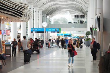 Yolcular havalimanında görünür dükkanlar ve tabelalar arasında geziniyorlar.