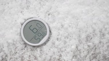 Bir dijital termometre taze kar yağışının ortasında serin sıcaklıkları gösterir.