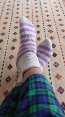 Yumuşak çizgili çoraplar evdeyken renkli bir halının üzerinde rahatça dinleniyor..