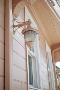 Bir duvar lambası pencereli pastel renkli bir eve asılmış..