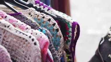 Tığ işi üstler ve aksesuarlar canlı bir pazar ortamında askıda asılı duruyor..