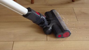 Bir insan ahşap zemindeki tozu temizlemek için elektrikli süpürge kullanır..