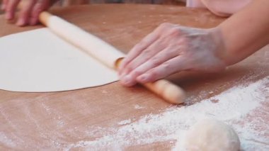 Hamur işlerini hazırlamak için ahşap bir yüzeye diz çöküp hamuru yuvarlıyor..