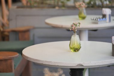 Küçük bir vazo sıcak bir kafe atmosferinde masanın üzerinde narin çiçekler tutar..