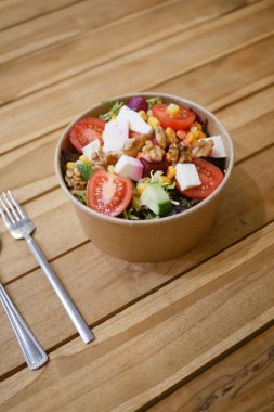 Taze malzemelerle dolu canlı bir salata kasesi ahşap bir masada oturur..