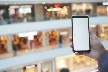 Bir insan alışveriş merkezinde dikilirken akıllı bir telefon tutar..