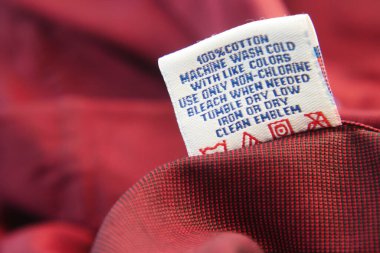 Etiket kırmızı pamuk kumaş için yıkama talimatları sağlar.
