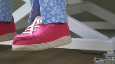 Pembe ortopedik ayakkabılı ve açık mavi pantolonlu kadınlar oturuyor. .