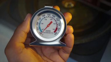 Bir insan fırının sıcaklığını kontrol etmek için termometre tutar..