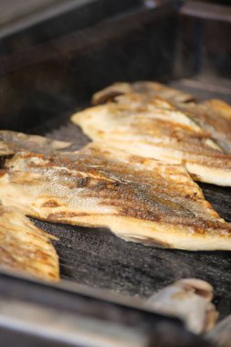 Balık filetoları ızgarada cızırdıyor, altın-kahverengi dokular ve tatlar sergiliyor..