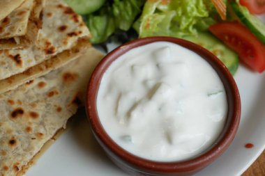 Kremalı yoğurt sosu ve taze sebzeyle servis edilen yuvarlak düz ekmek.