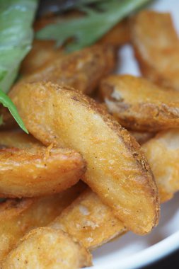 Taze yeşil garnitürlerin yanında altın patates dilimleri servis edilir..