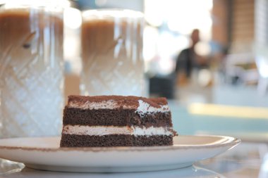 Bir dilim çikolatalı kek bir tabakta buzlu kahve içeceklerinin yanında oturur..