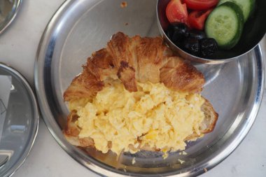 Çırpılmış yumurtalarla dolu kruvasan ve yanında taze salata..