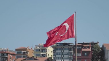 Renkli binaları olan bir şehrin üzerinde gururla dalgalanan büyük bir Türk bayrağı.