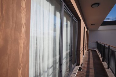 Parlak balkon, sürgülü cam kapılar ve gün ışığında ahşap güverte..