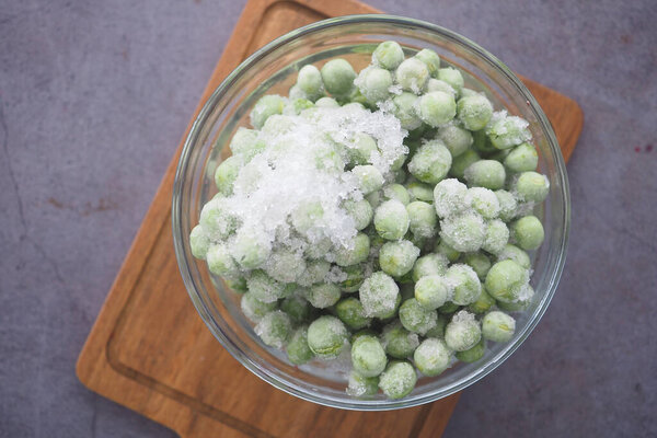 Чаша с замороженным зеленым горохом, увенчанная льдом, сидит на разделочной доске..