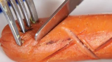 Bir çatal ve bıçak, canlı bir sosisi tabakta keser..