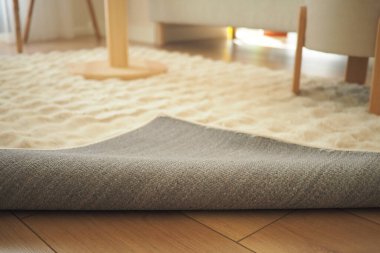 Gri halı, sıcak, davetkar bir yaşam alanının ahşap zemininde yuvarlanır..