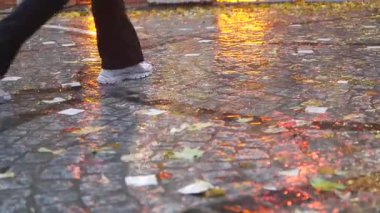 İnsanlar alacakaranlıkta yağmurlu bir sokakta su birikintilerinde gezinirler..