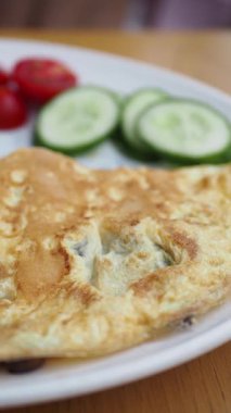 Dilimlenmiş salatalık ve vişneli domatesle servis edilen lezzetli omletin tadını çıkarın..