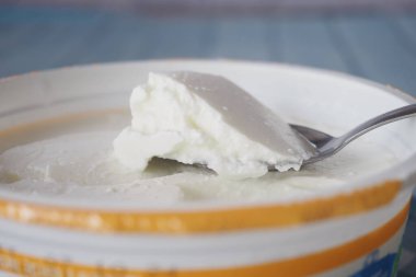 Bir kaşık dolusu yumuşak yoğurt bir kasenin içindeki kremalı dokuda duruyor..