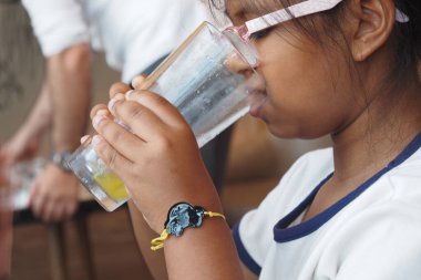 Gözlüklü genç bir kız evdeyken uzun bir bardaktan su içiyor..