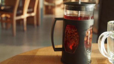 Sıcak bir kafe, ahşap bir masada çay ütüleyicisi barındırır, içeri güneş ışığı girer..