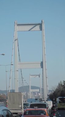 Araçlar mavi gökyüzünün altında büyük bir köprüden geçiyor..