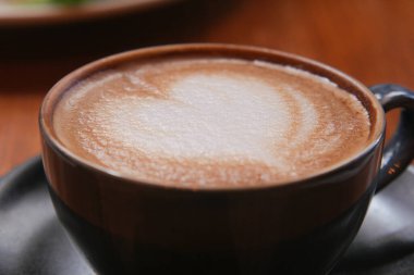 Sıcak bir kafe atmosferinde kalp şeklinde köpük desenli kremalı latte..