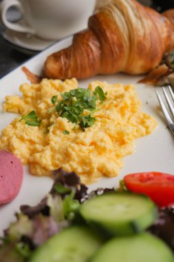 Çırpılmış yumurta, üstüne ot, salata ve kruvasan..