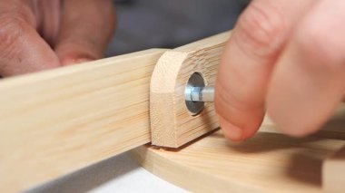Bir kişi ahşap çerçeveyi el aletleri ve vidalar kullanarak birleştirir.