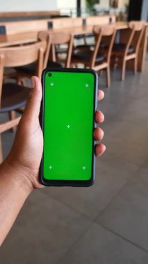 Bir kişi şık bir kafede boş ekranlı mobil bir cihaz gösterir.